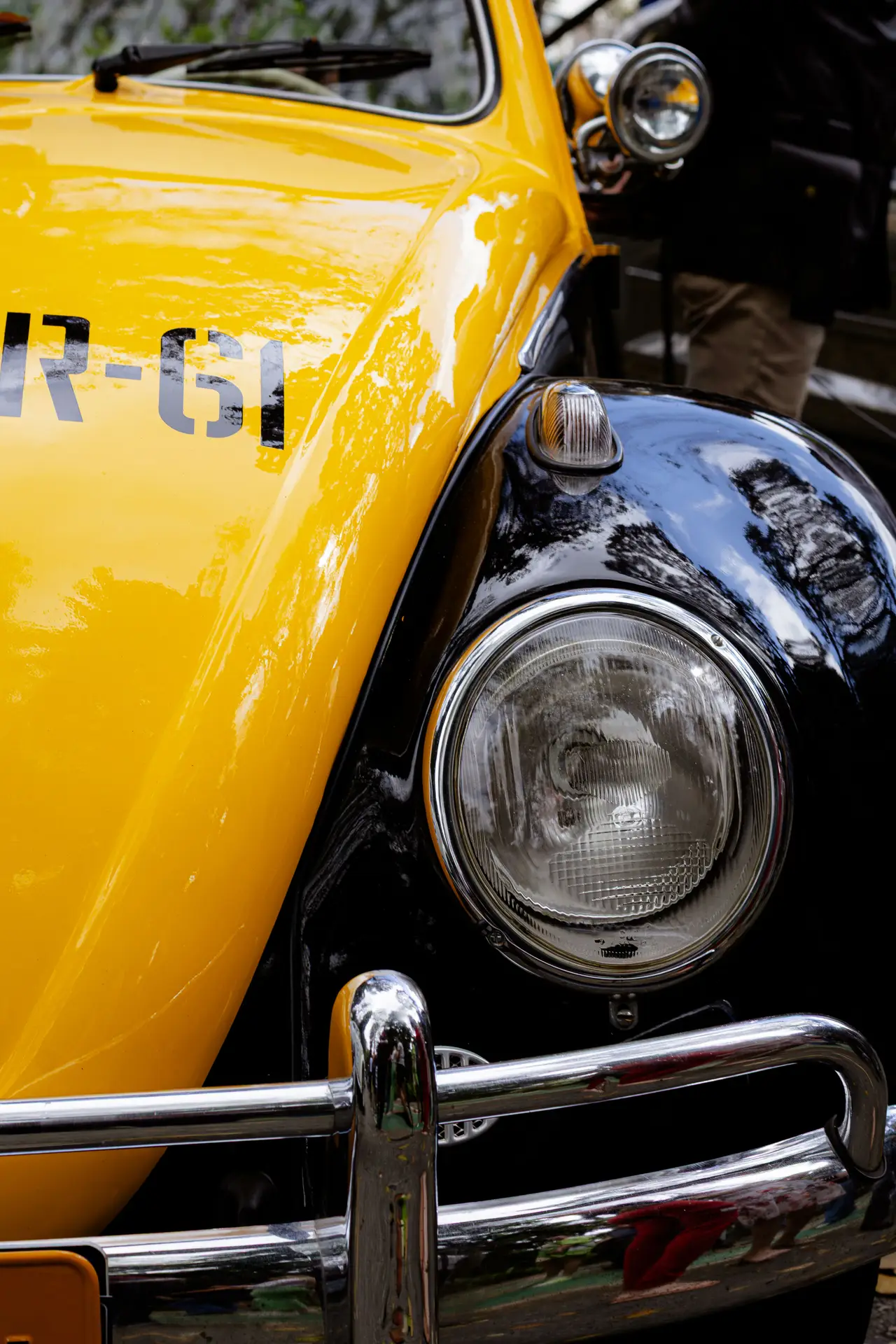 Close-up of a classic yellow and black VW Beetle's front headlight and bumper.